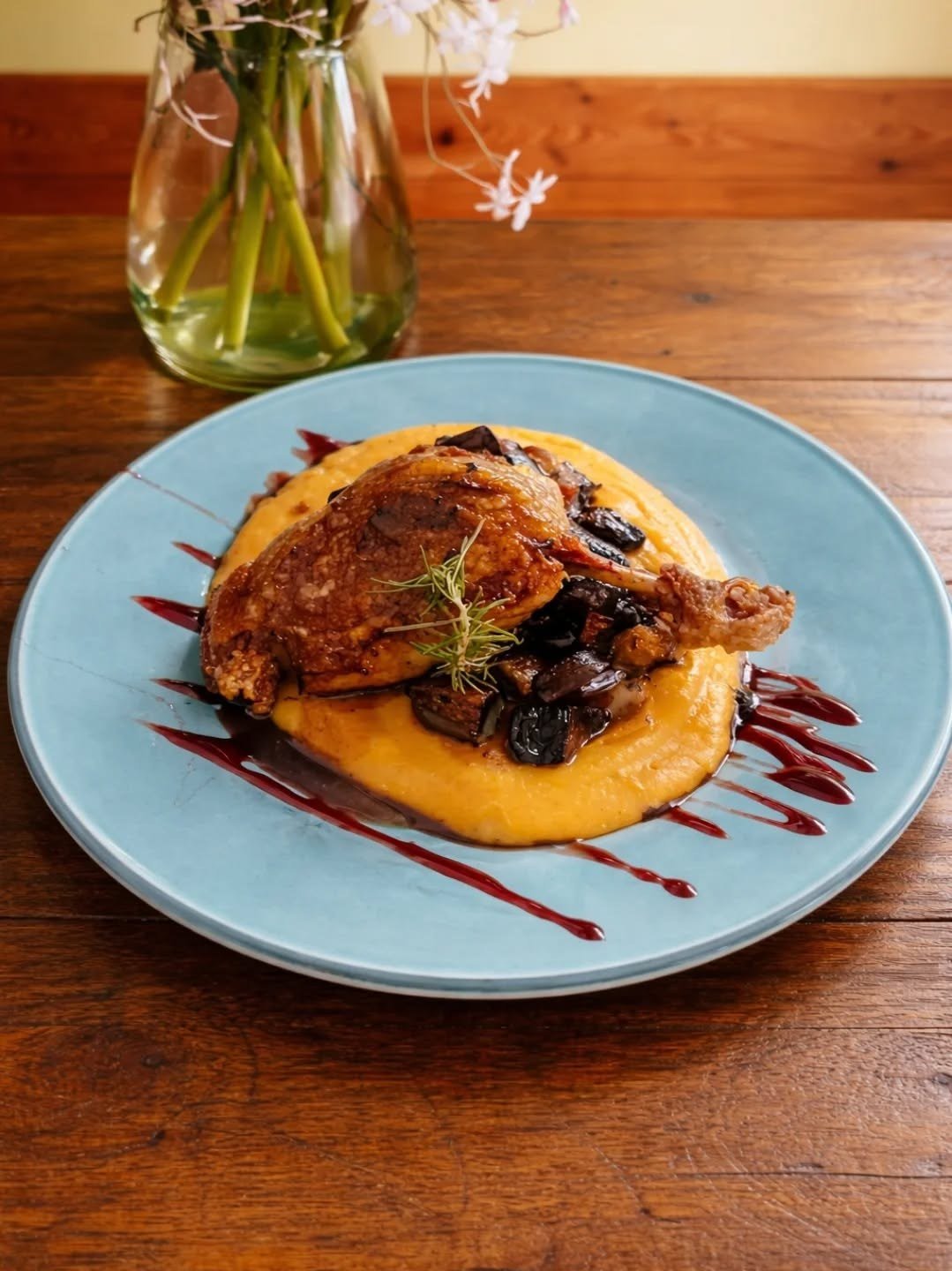 Coxa de pato confitada sobre puré, num prato azul em mesa de madeira