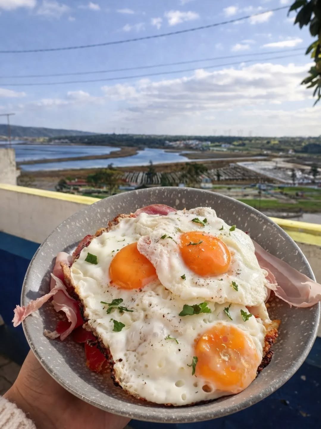 Prato de ovos estrelados sobre batata e presunto, com o rio e a planície ao fundo
